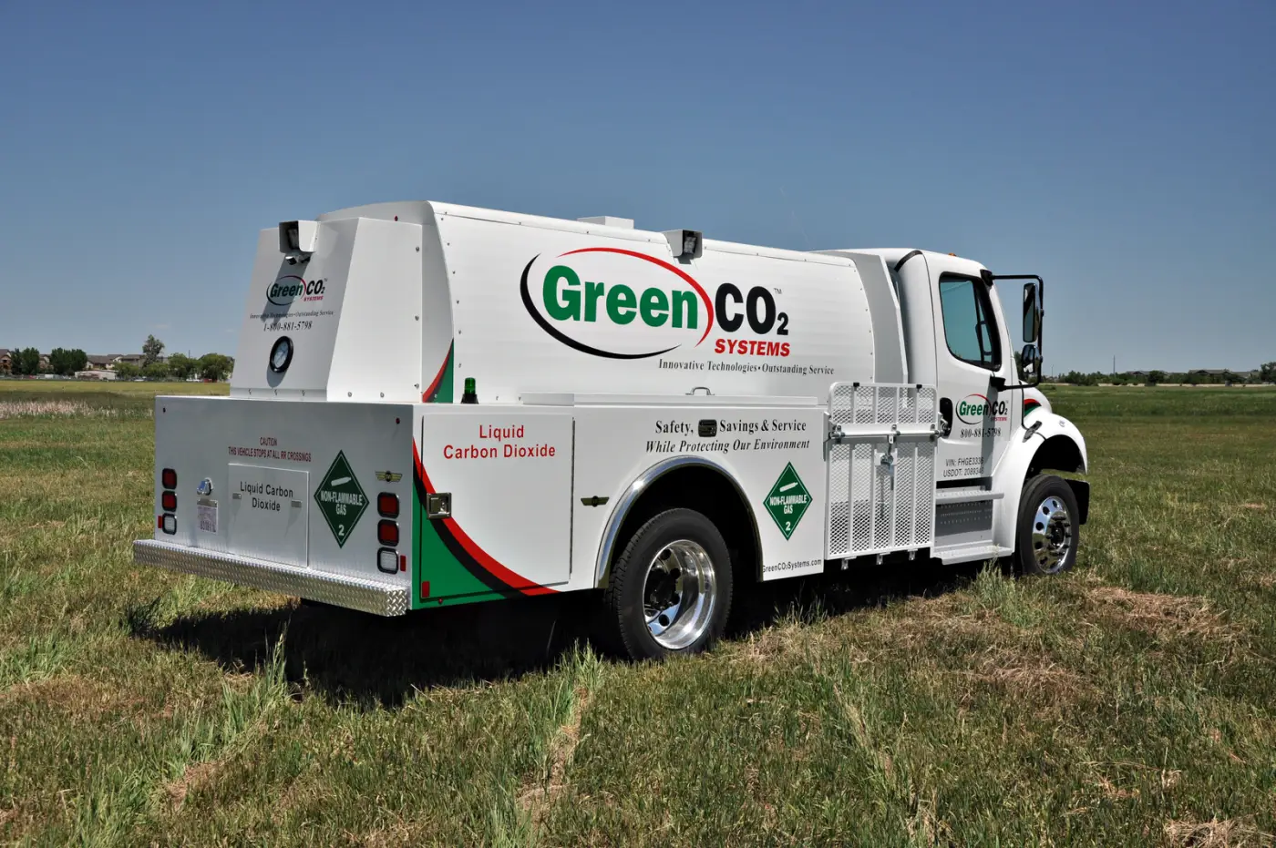 A white Green CO2 Systems bulk delivery truck marked Liquid Carbon Dioxide, parked on grass under a blue sky.