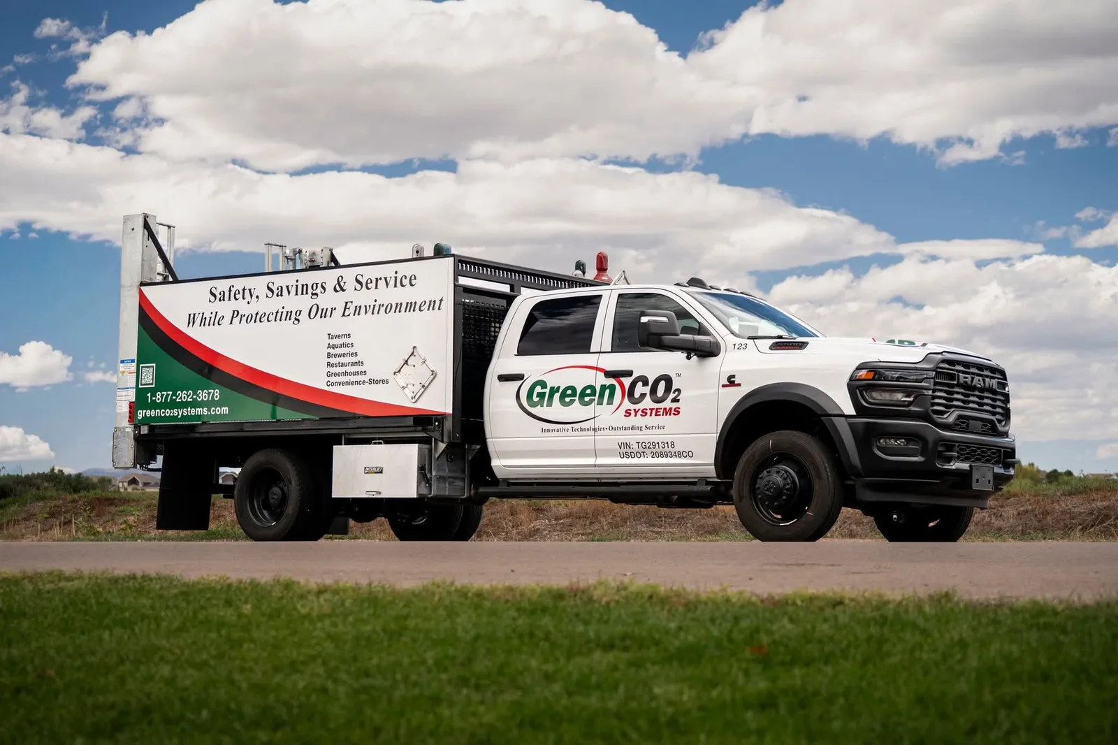 A Green CO2 Systems service pickup with a branded flatbed, parked beside a field under a cloudy sky.