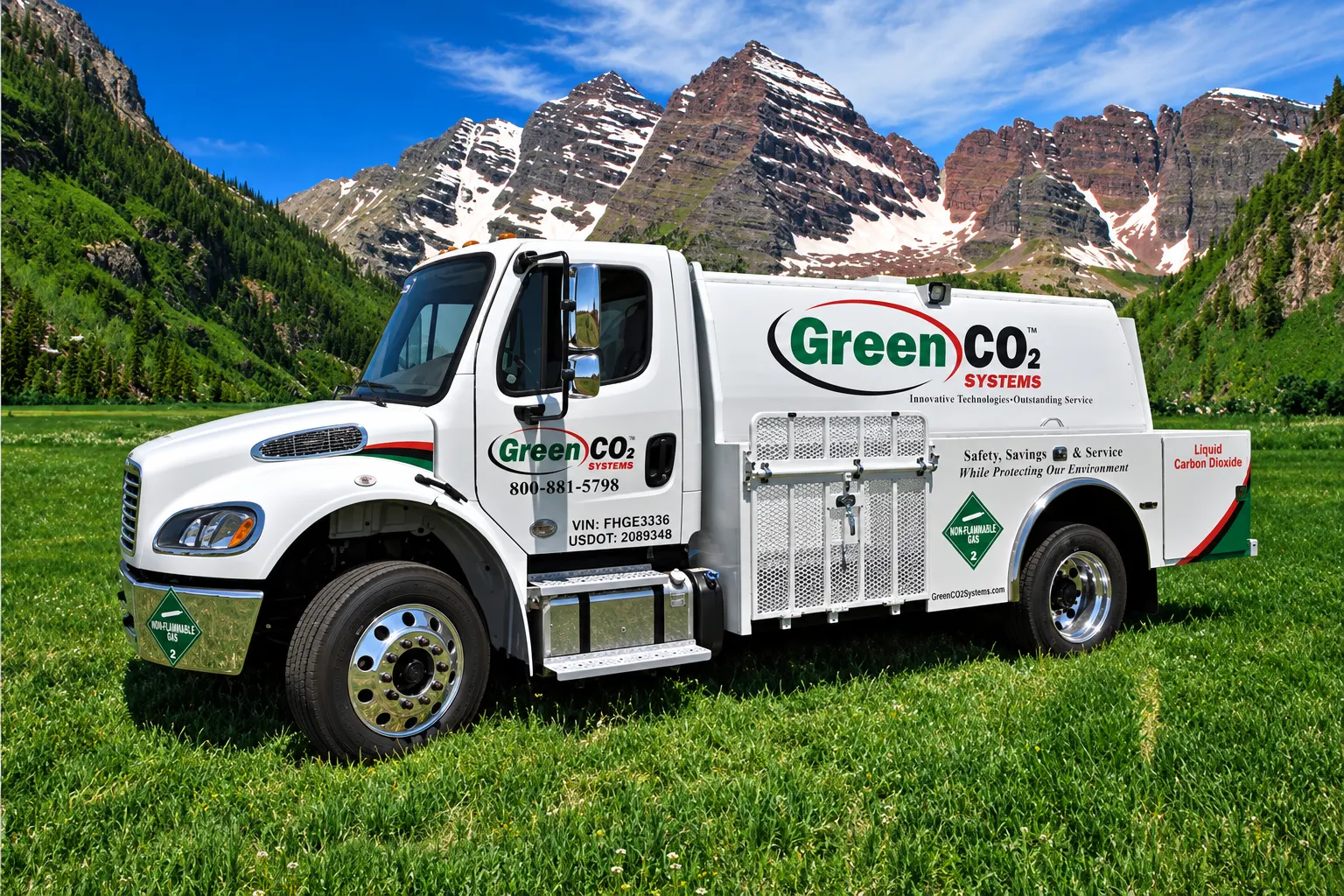 A white Green CO2 Systems bulk delivery truck parked on a green meadow in front of snow-streaked Colorado mountain peaks.